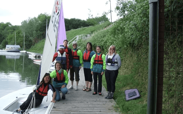 Things to do in East Cambs in Spring - Ely Sailing Club Open Day. Group in lifejackets smiling near small sailboat.