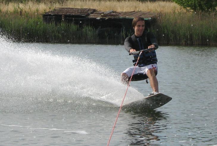 Things to do in East Cambridgeshire - Wakeboarding. Image of smiling man in life vest wake boarding on water